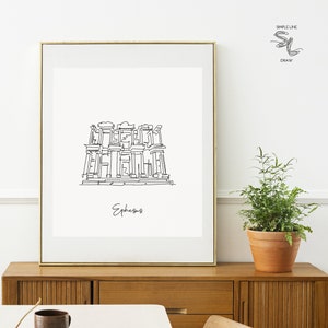 Puede incluir: Un dibujo en blanco y negro de la antigua ciudad de Éfeso, Turquía. El dibujo está enmarcado en un marco dorado y colgado en una pared blanca sobre una cómoda de madera.