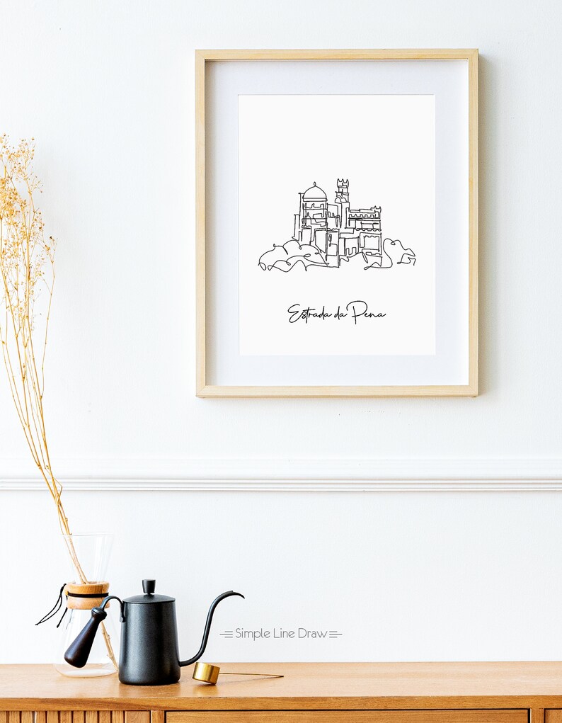 May include: A black and white line drawing of the Pena Palace in Sintra, Portugal. The drawing is framed in a light wood frame and hanging on a white wall. The text "Estrada da Pena" is written below the drawing.