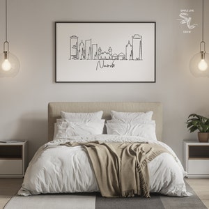 Puede incluir: Un dibujo lineal en blanco y negro enmarcado del horizonte de Nairobi cuelga sobre una cama con ropa de cama blanca y una manta beige. El texto "Nairobi" est&aacute; escrito debajo del horizonte. La habitaci&oacute;n est&aacute; decorada con l&aacute;mparas modernas y mesitas de noche.