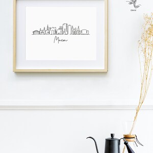 Puede incluir: Un dibujo en blanco y negro de la l&iacute;nea del horizonte de Macon, Georgia, enmarcado. El dibujo est&aacute; hecho en un estilo de l&iacute;nea simple e incluye el nombre de la ciudad debajo del horizonte.