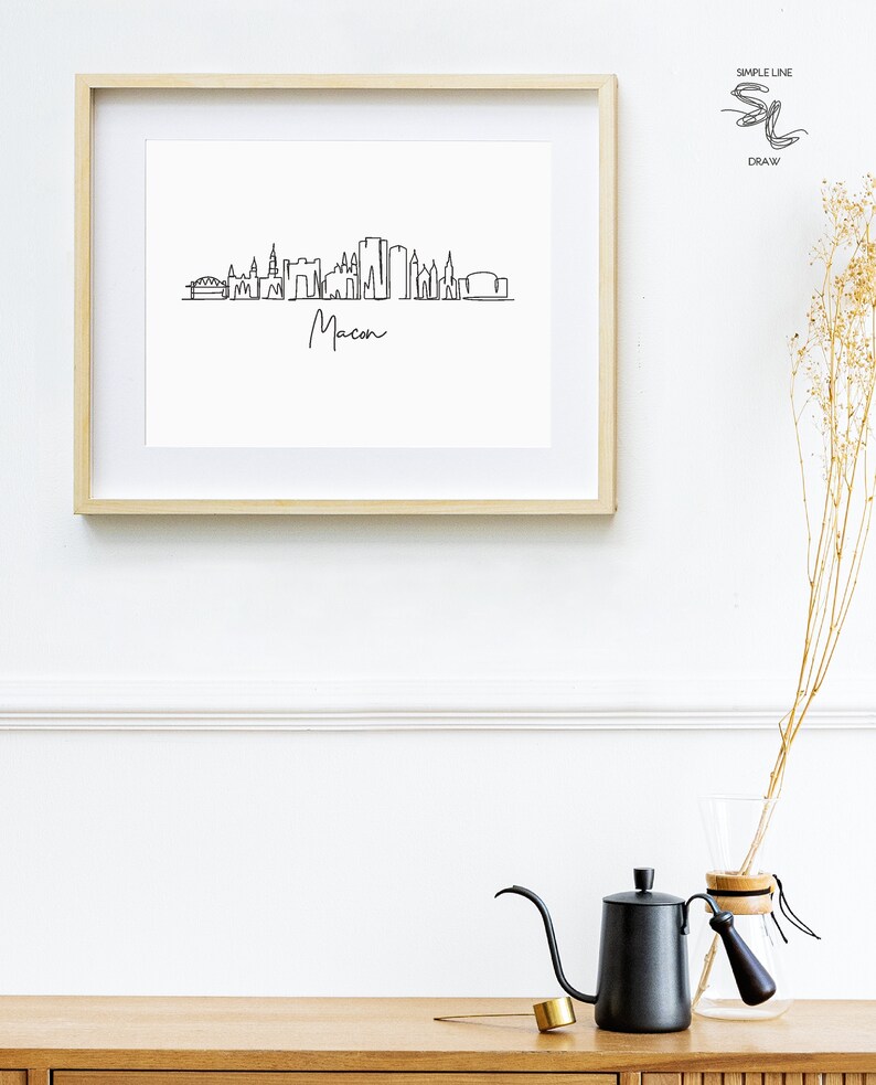 Puede incluir: Un dibujo en blanco y negro de la l&iacute;nea del horizonte de Macon, Georgia, enmarcado. El dibujo est&aacute; hecho en un estilo de l&iacute;nea simple e incluye el nombre de la ciudad debajo del horizonte.
