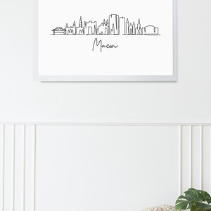 Puede incluir: Un dibujo en blanco y negro de la l&iacute;nea del horizonte de Macon, Georgia. El dibujo incluye un puente, varios edificios y la palabra "Macon" escrita en cursiva.