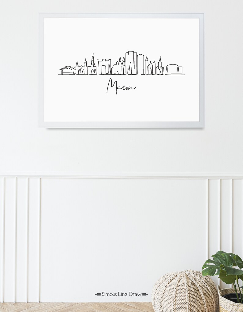 Puede incluir: Un dibujo en blanco y negro de la l&iacute;nea del horizonte de Macon, Georgia. El dibujo incluye un puente, varios edificios y la palabra "Macon" escrita en cursiva.