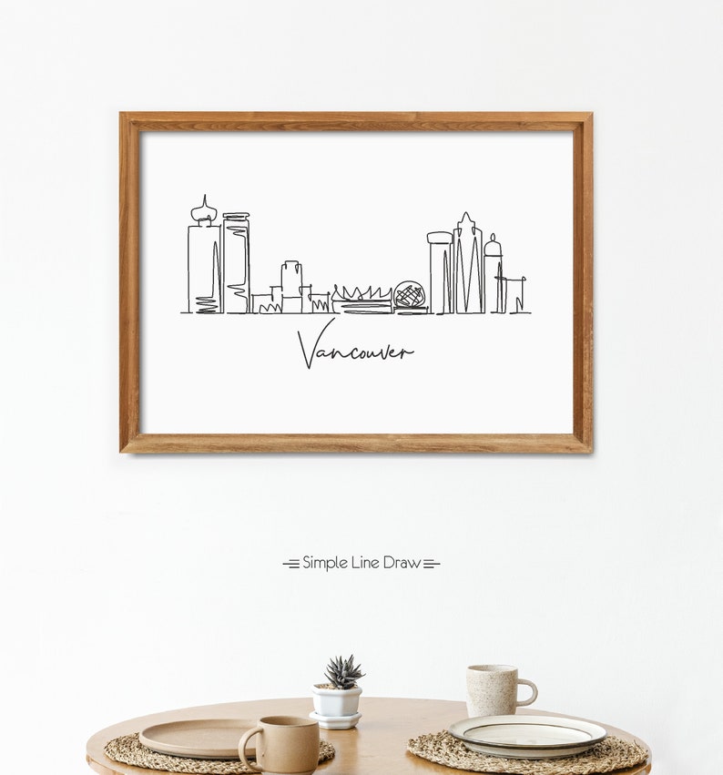 Puede incluir: Un dibujo en blanco y negro de la l&iacute;nea del horizonte de Vancouver enmarcado. El dibujo est&aacute; en un estilo de l&iacute;nea simple e incluye el texto "Vancouver". El marco es de madera marr&oacute;n.