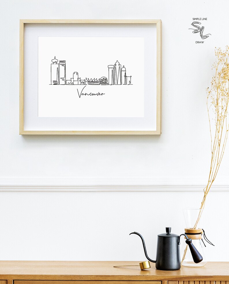 Puede incluir: Un dibujo en blanco y negro de la l&iacute;nea del horizonte de Vancouver enmarcado. El dibujo est&aacute; en un estilo de l&iacute;nea simple e incluye el texto "Vancouver" en la parte inferior.