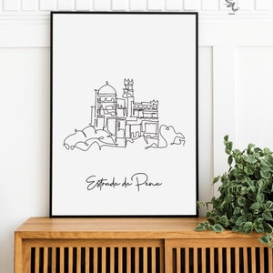 May include: Black and white line art print of the Pena Palace in Sintra, Portugal. The print is framed and hanging on a wall above a wooden cabinet. The text "Estrada da Pena" is written below the image.