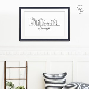 May include: A black framed print of a line drawing of the Wilmington skyline. The drawing is in a simple line style and includes the text "Wilmington".