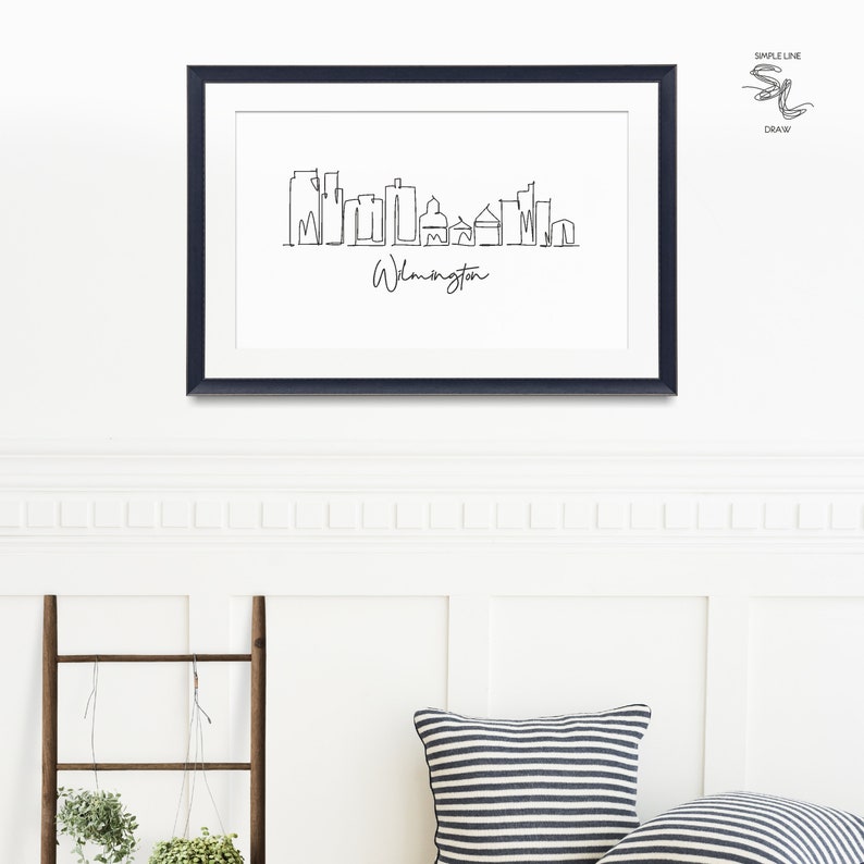 May include: A black framed print of a line drawing of the Wilmington skyline. The drawing is in a simple line style and includes the text "Wilmington".