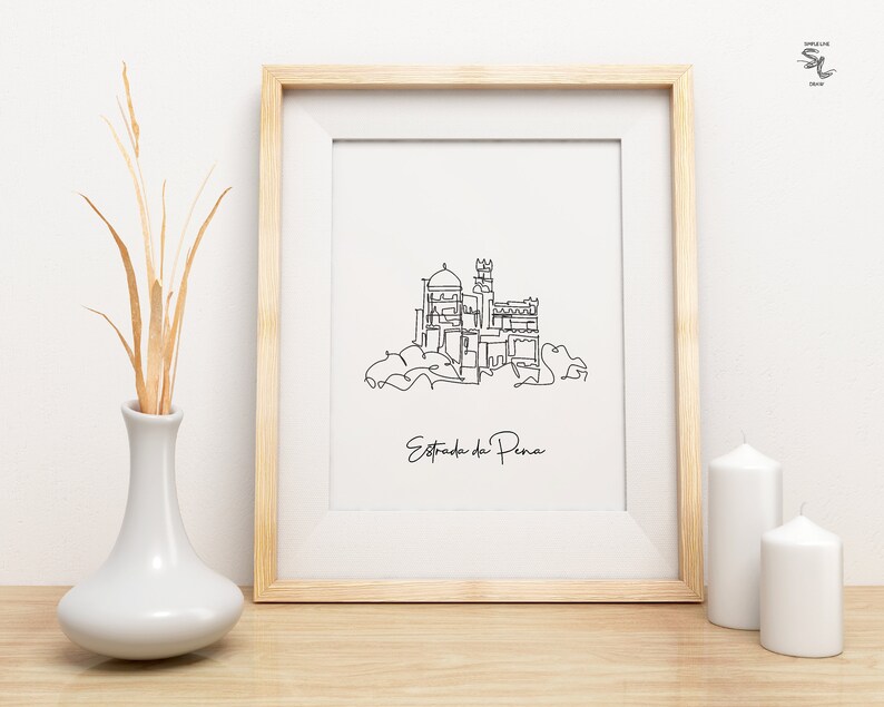 May include: A black and white line drawing of the Pena Palace in Sintra, Portugal. The drawing is framed in a light wood frame and is hanging on a white wall. The text "Estrada da Pena" is written below the drawing.
