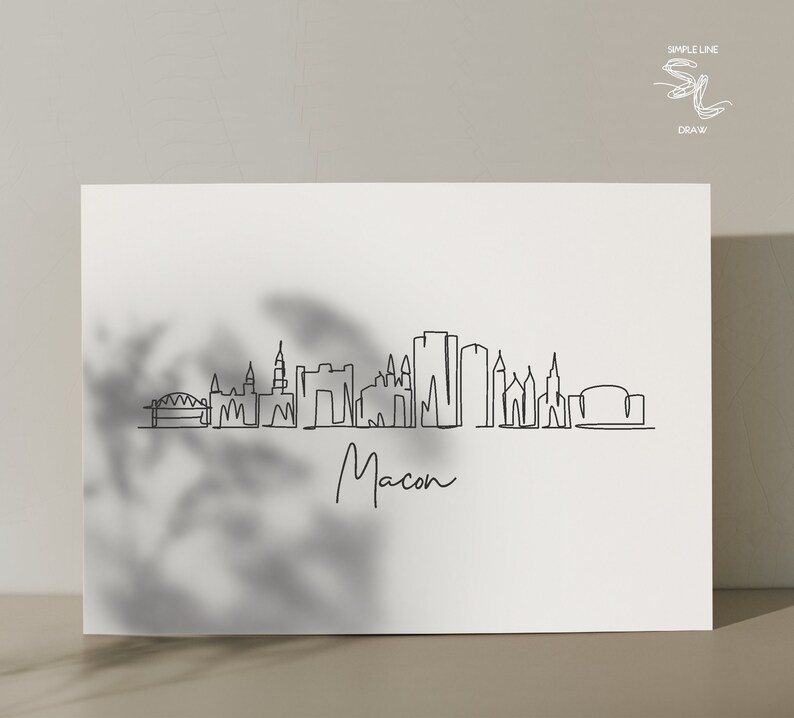Puede incluir: Un dibujo en blanco y negro de la l&iacute;nea del horizonte de Macon, Georgia. El dibujo incluye los edificios m&aacute;s reconocibles de la ciudad, incluido el Macon City Auditorium y el Macon Coliseum. El dibujo est&aacute; titulado "Macon" en cursiva.