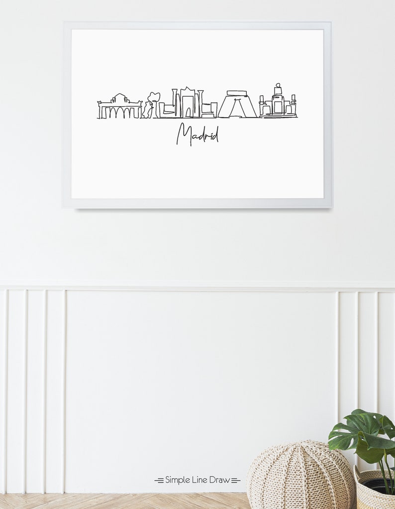 May include: A framed minimalist line drawing of the Madrid skyline in black against a white background. The word "Madrid" is written in cursive below the skyline. The frame is white. The bottom of the image has the text "Simple Line Draw".