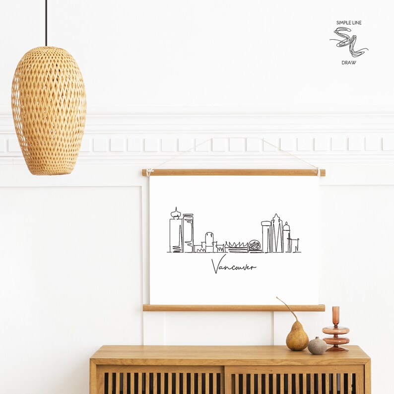Puede incluir: Un dibujo en blanco y negro de la l&iacute;nea del horizonte de Vancouver con la palabra "Vancouver" escrita debajo. El dibujo est&aacute; enmarcado y colgado en una pared blanca sobre un armario de madera.