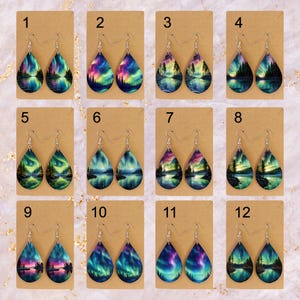 May include: Twelve pairs of teardrop-shaped earrings with a variety of aurora borealis designs. Each pair features a silver hook and a painted wooden teardrop. The earrings are numbered 1 through 12.