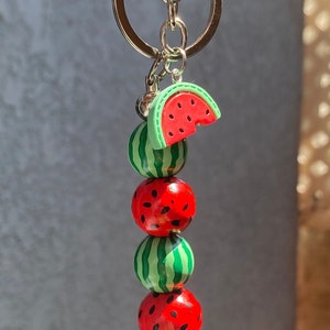 May include: A watermelon keychain with a silver key ring. The keychain features a watermelon slice charm and three round watermelon beads.