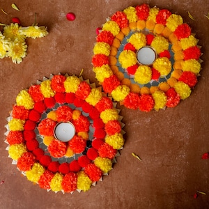 May include: Two circular floral arrangements with yellow and orange marigold pom-poms surrounding a mirrored center with a small candle holder.