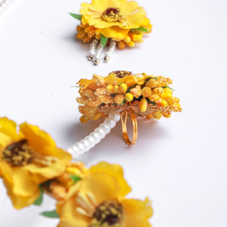 May include: A set of yellow flower jewelry with a ring, a bracelet, and two hair clips. The jewelry is made of artificial flowers and pearls.
