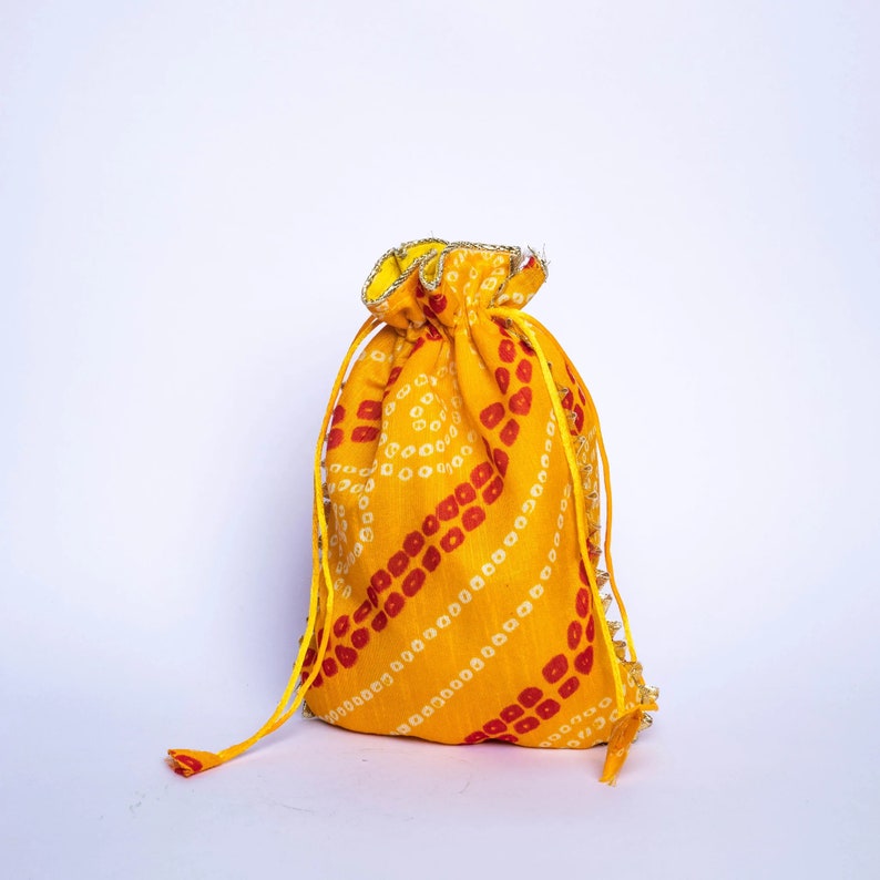 Pu&ograve; includere: Una borsa a cordoncino gialla con un motivo rosso e bianco. La borsa ha un bordo dorato ed &egrave; fatta di tessuto.