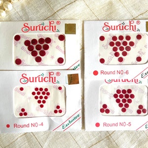 May include: Four packs of red round adhesive bindis, each pack contains a different number of bindis. The packs are labeled "Suruchi" and "Exclusive" and have the numbers "NO-4", "NO-5", and "NO-6" printed on them.