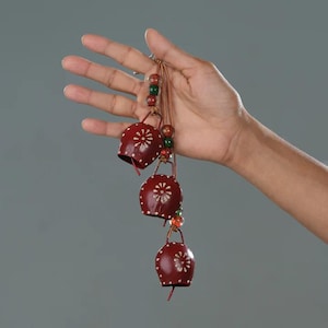 May include: A set of three red cowbells with white floral designs, strung together with brown cord and colorful beads.