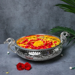May include: A silver bowl with ornate detailing, featuring a floral arrangement of red and yellow petals floating in water.