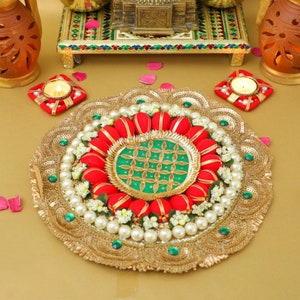 May include: A gold decorative plate with a green and gold center surrounded by red fabric flowers and white pearls. The plate is on a gold background.