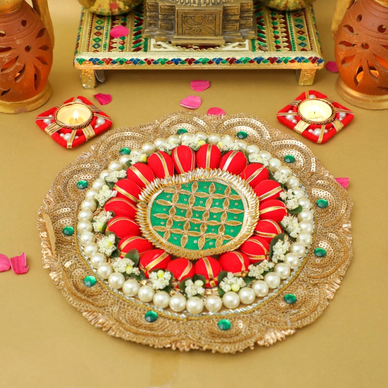 May include: A gold decorative plate with a green and gold center surrounded by red fabric flowers and white pearls. The plate is on a gold background.