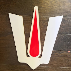May include: A white, three-pointed crown with a red, pointed teardrop shape in the center.