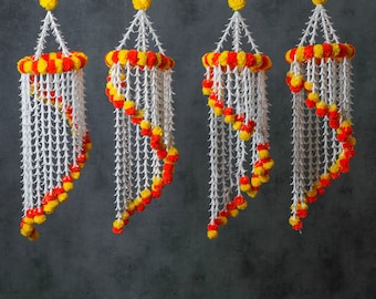May include: Four decorative hanging ornaments. Each ornament features a white, spiky structure with a spiral of red and yellow pom-poms. The top and bottom of each ornament are adorned with a ring of alternating red and yellow pom-poms.