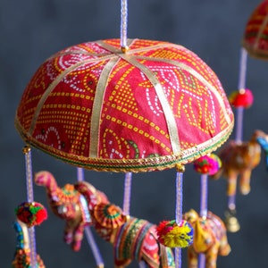 May include: A colorful mobile with red, yellow, and white fabric elephants hanging from a red and gold fabric canopy. The canopy is decorated with a white and gold pattern.