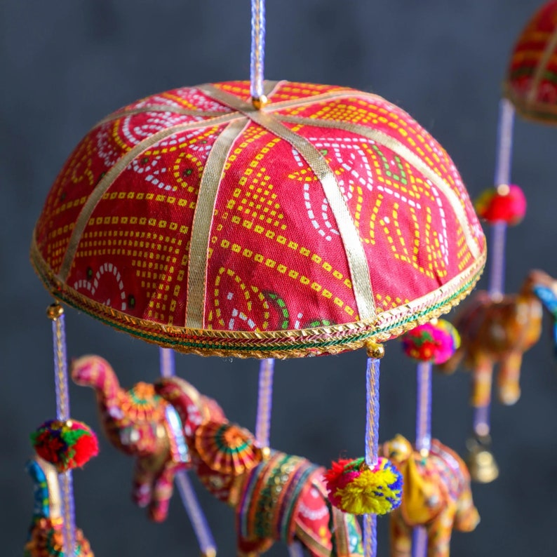 May include: A colorful mobile with red, yellow, and white fabric elephants hanging from a red and gold fabric canopy. The canopy is decorated with a white and gold pattern.