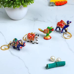 May include: A collection of colorful, miniature animal figurines, including an elephant, a camel, a parrot, and a cow, each with a gold-colored keychain ring. The figurines are painted with intricate patterns in red, blue, green, and white.
