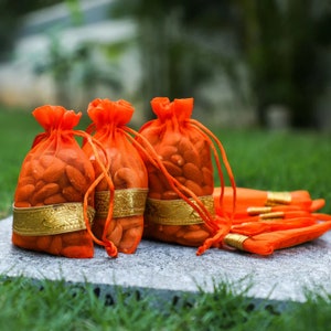 May include: Four orange drawstring bags filled with almonds, with a gold trim around the top of each bag. The bags are sitting on a gray stone surface.