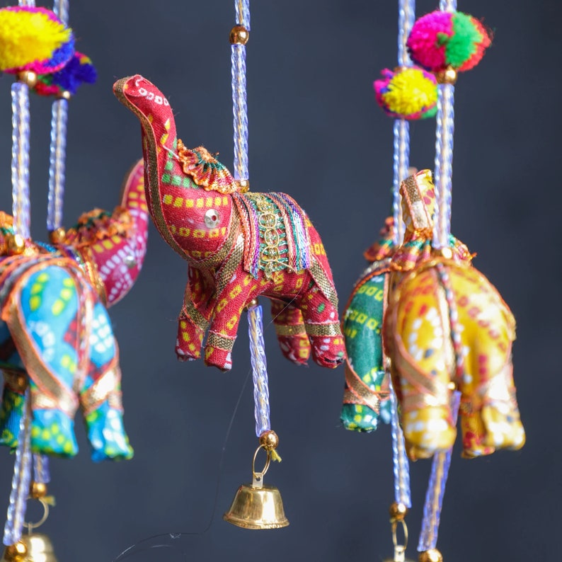 May include: A colorful hanging mobile with four fabric elephants, each with a different pattern and color. The elephants are attached to strings with bells at the bottom.