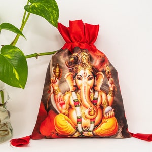 May include: Red drawstring bag with a printed image of the Hindu deity Ganesha. The bag has a gold tassel on each side.