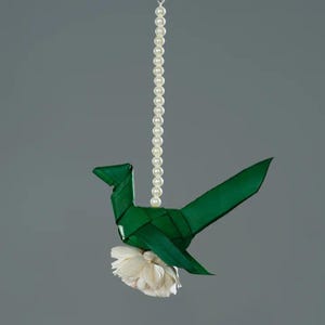 May include: A green origami bird with a white flower hanging from a string of white pearls.