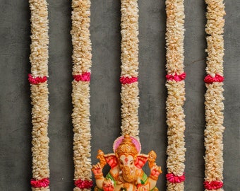 May include: A colorful statue of the Hindu deity Ganesha, sitting in a meditative pose. The statue is decorated with flowers and is surrounded by garlands of white flowers.