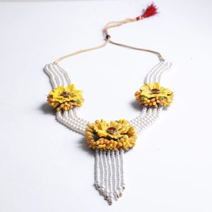 May include: A white pearl necklace with three yellow flower accents. The necklace has a tassel of pearls at the bottom.