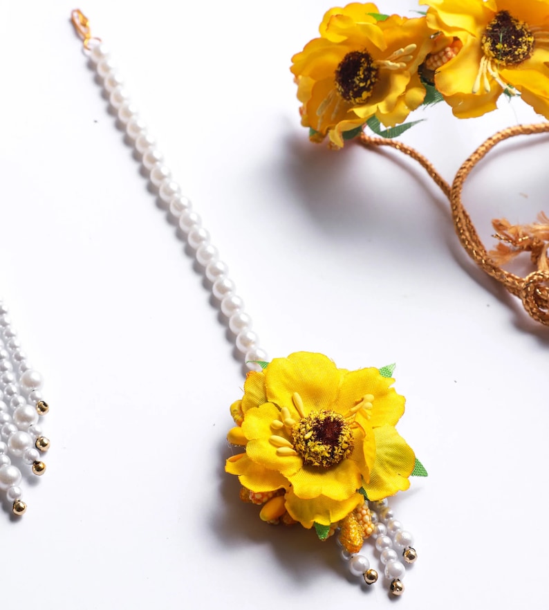 May include: A set of yellow flower hair accessories with pearl strands. The set includes a headband and a hair clip.