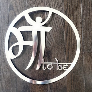 May include: A silver metal circle with the words "to be" and a stylised Hindi word in the centre.
