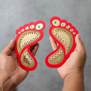 May include: Two red, decorative, foot-shaped plaques with gold and green embellishments. The plaques are decorated with a pattern of circles, triangles, and paisley shapes.