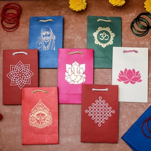 Puede incluir: Una colecci&oacute;n de coloridas bolsas de regalo de papel con varios dise&ntilde;os religiosos y geom&eacute;tricos. Las bolsas son en tonos de rojo, azul, verde, rosa y blanco. Cada bolsa presenta una imagen diferente, incluyendo una flor de loto, el s&iacute;mbolo Om y una deidad.