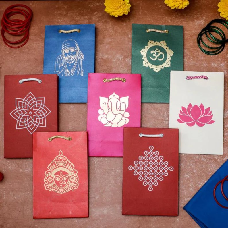 Puede incluir: Una colecci&oacute;n de coloridas bolsas de regalo de papel con varios dise&ntilde;os religiosos y geom&eacute;tricos. Las bolsas son en tonos de rojo, azul, verde, rosa y blanco. Cada bolsa presenta una imagen diferente, incluyendo una flor de loto, el s&iacute;mbolo Om y una deidad.