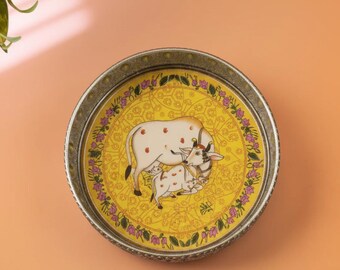 May include: Round decorative tray with a yellow center featuring a cow and calf illustration. The tray has a silver-colored rim and a floral border with pink flowers. The cow has red spots.