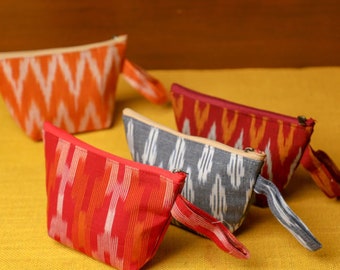 May include: Five colorful zippered pouches with a geometric pattern. The pouches are made of fabric and have a cream-colored lining. The pouches are arranged in a row on a yellow surface.