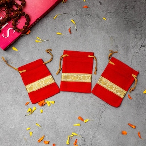 May include: Three red velvet pouches with gold trim and drawstrings. The pouches are on a gray textured surface.