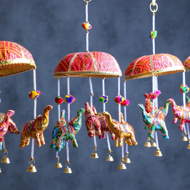 May include: A colorful mobile with red, gold, and white fabric umbrellas and hanging elephant ornaments. The elephants are decorated with colorful embroidery and beads.