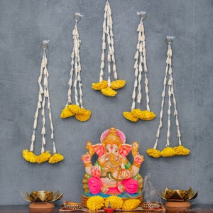May include: A colorful statue of the Hindu deity Ganesha, decorated with garlands of yellow flowers, sits on a table with two golden candle holders and a small red candle.
