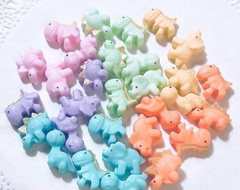 May include: A collection of pastel-colored dinosaur figurines with gold accents. The dinosaurs are arranged in a circle on a white surface.