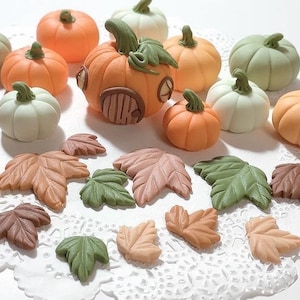 May include: A collection of miniature fall-themed decorations, including pumpkins, gourds, and leaves. The pumpkins are in various shades of orange, green, and white. The leaves are in shades of brown, green, and orange.