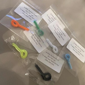 May include: A selection of belly button brushes, each in a clear plastic bag. The brushes are in various colours: orange, green, yellow, black, white, and blue. Each bag has a label with the text "A Belly Button Brush, Just For You, To Make Your Belly Button Clean And New."